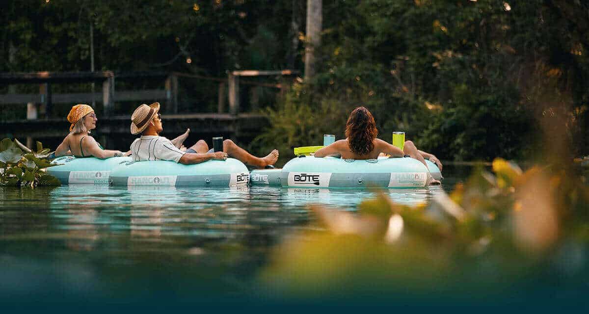 Four people tubing on a river in BOTE Inflatable Hangout FLOATube Classic tubes with the Inflatable Hangout Float Kula Bar, and MAGNEPOD Magnetic Retention System MAGNETumbler drinkware.