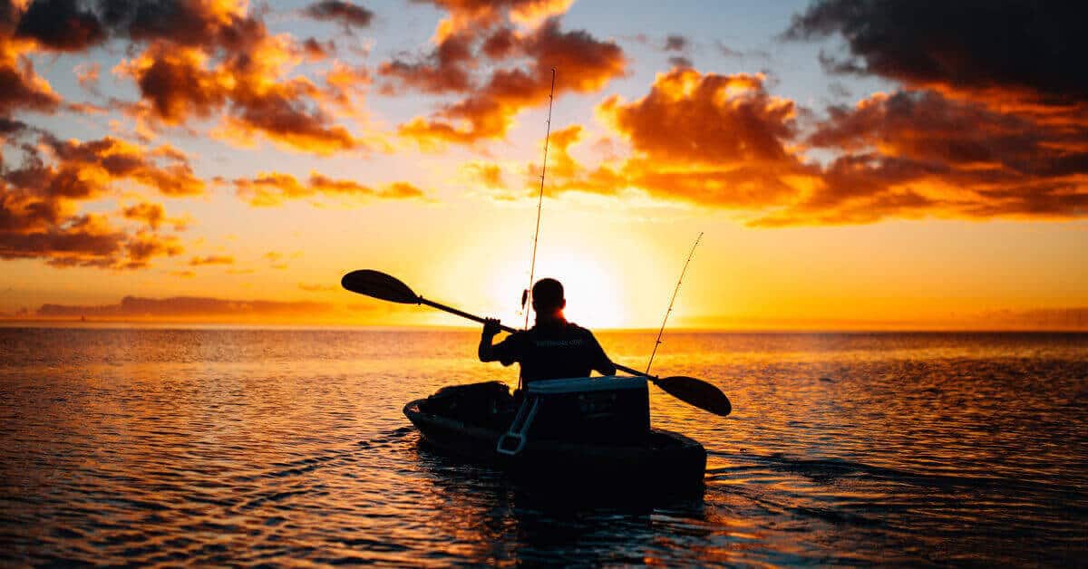 Kayak fisherman paddling into an ocean sunset.